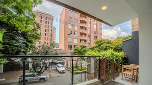 A balcony with a view of a street, a parked car, and a building with multiple floors and balconies. - w Spacious 3BR w Outdoor Dining Terrace in Laureles (Medellín)