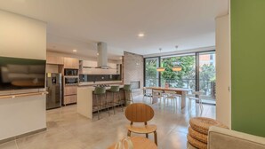 A modern kitchen with a central island, bar stools, and a dining area with a table and chairs. - w Spacious 3BR w Outdoor Dining Terrace in Laureles (Medellín)