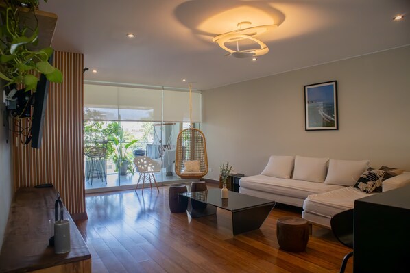 A modern living room with a white sofa, a glass coffee table, and a hanging chair. - w Atonishing 1BR With Terrace in Barranco (Lima)