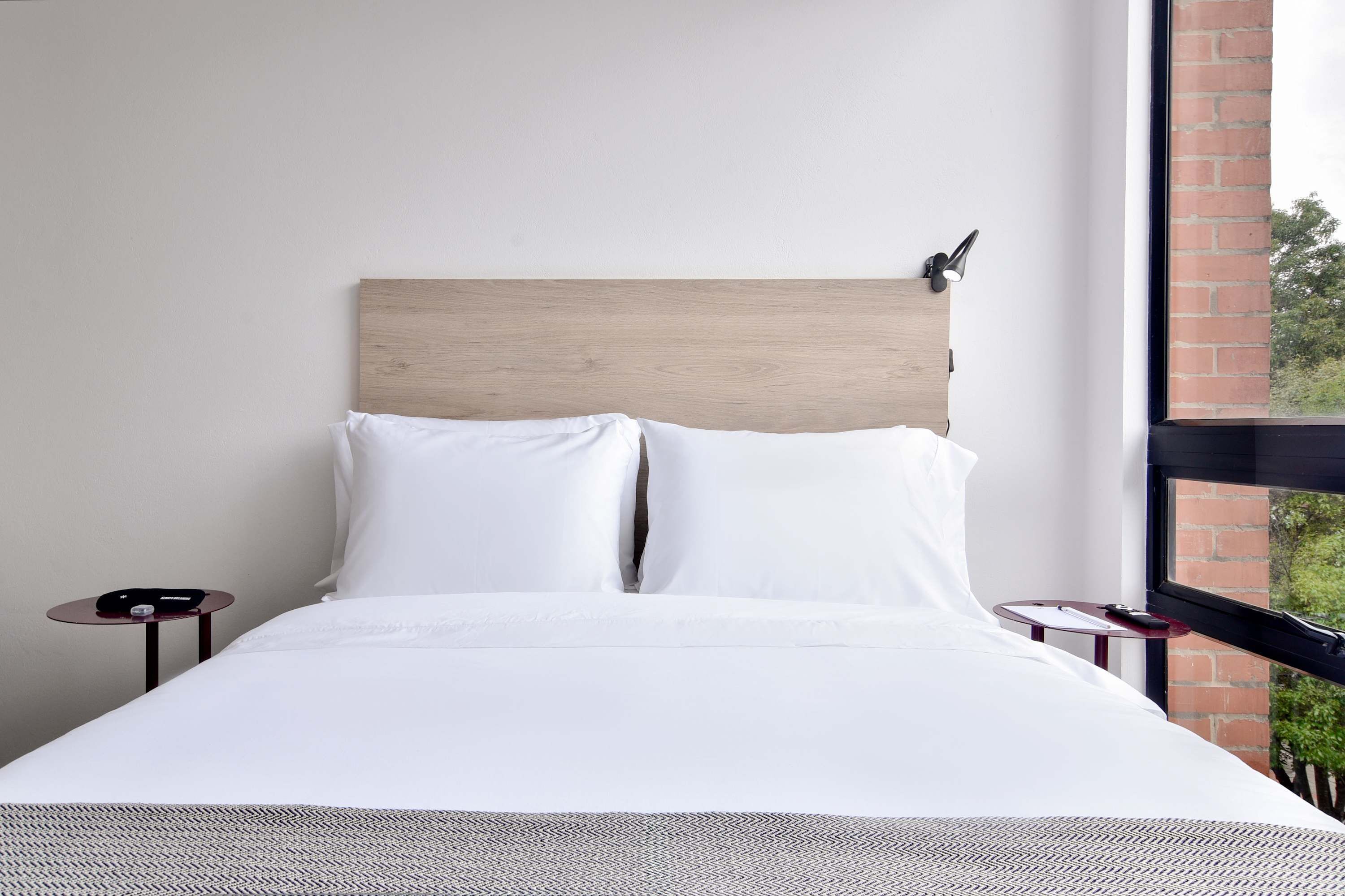 A neatly made bed with white linens, a wooden headboard, and two bedside tables with electronic devices.