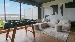A modern living room with a foosball table, a large window, and a sectional sofa. - w Impressive 2BR With Balcony in Miraflores (Lima)