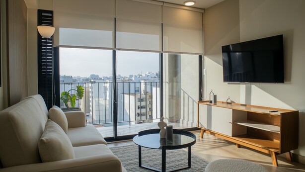 A modern living room with a sofa, a coffee table, a TV, and a view of the city. - w Impressive 2BR With Balcony in Miraflores (Lima)