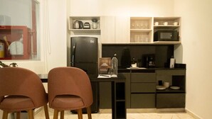 A modern kitchen with a black refrigerator, wooden chairs, and a marble countertop.
