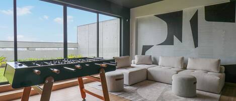 A modern living room with a foosball table, a large window, and a sectional sofa.