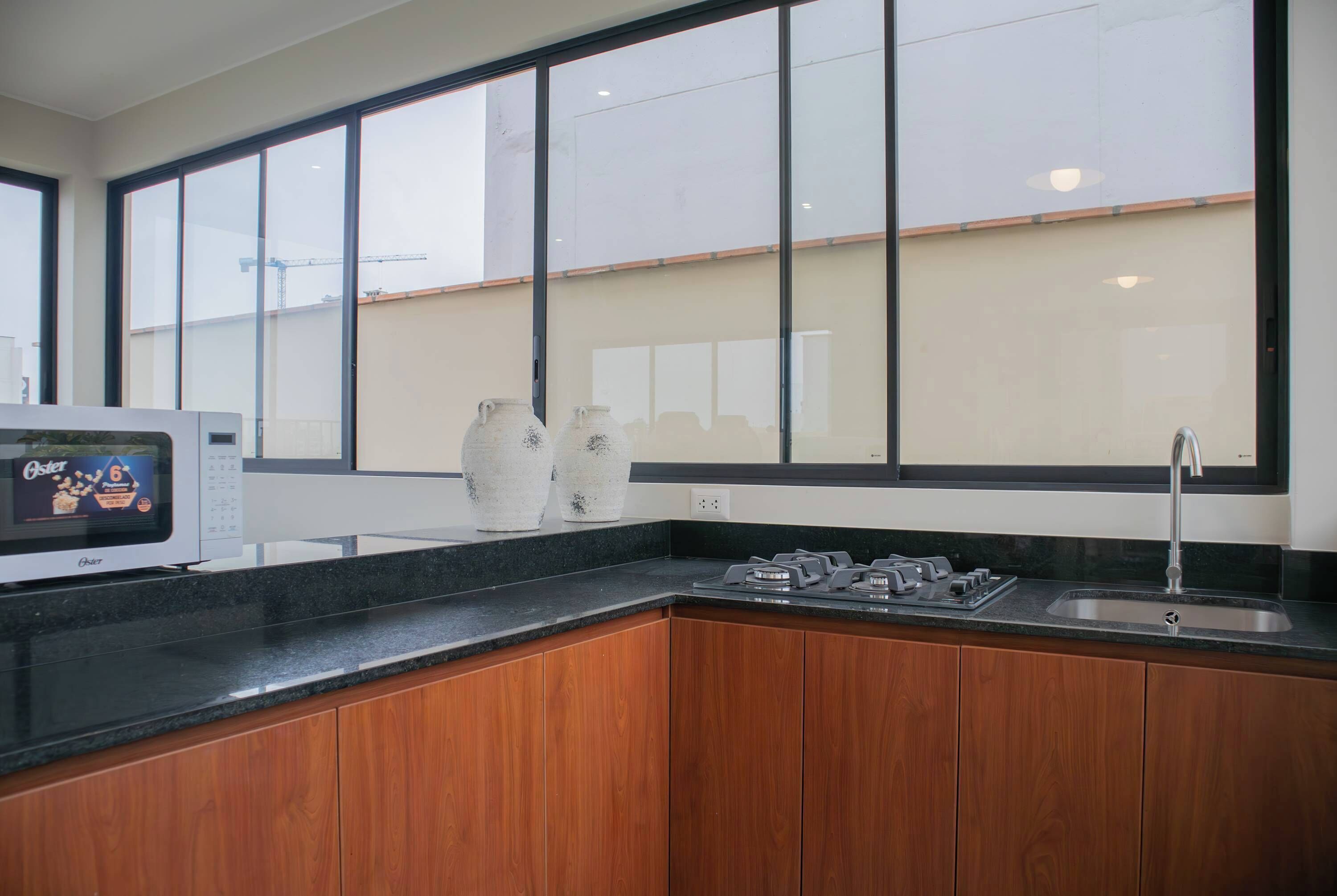 A modern kitchen with a large window, wooden cabinets, a built-in oven, and a stainless steel sink.
