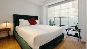 A bedroom with a large bed, a bedside table, a nightstand, a window with blinds, and a potted plant. - w Amazing 2BR in Roma Norte (Mexico City)