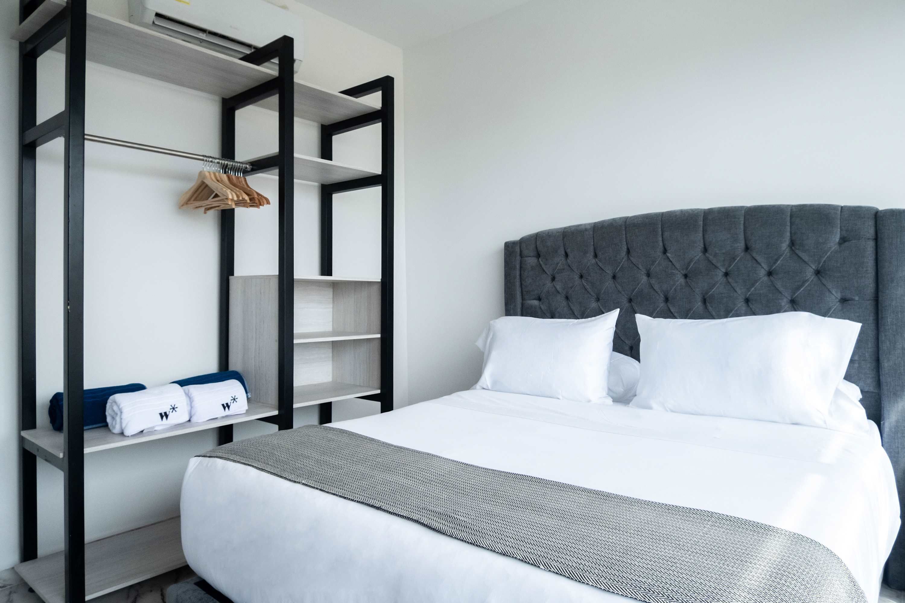 A modern hotel room with a large bed, a grey upholstered headboard, and a built-in wardrobe with hanging space.