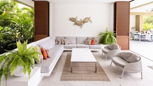 A modern living room with a sectional sofa, a coffee table, and two armchairs. There is a decorative wall piece above the sofa and a large window providing a view of greenery outside. - w Mind-blowing 4BR Villa w Pool at Mesa de Yeguas (Anapoima)