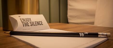A notebook with a pencil, a card that reads "ENJOY THE SILENCE," and a pair of earplugs on a wooden surface.