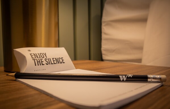 A notebook with a pencil, a card that reads "ENJOY THE SILENCE," and a pair of earplugs on a wooden surface.