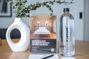 Une brochure présentant des opportunités d’investissement immobilier dans le domaine de la location de courte durée, une bouteille d’eau transparente et un vase blanc avec une plante.