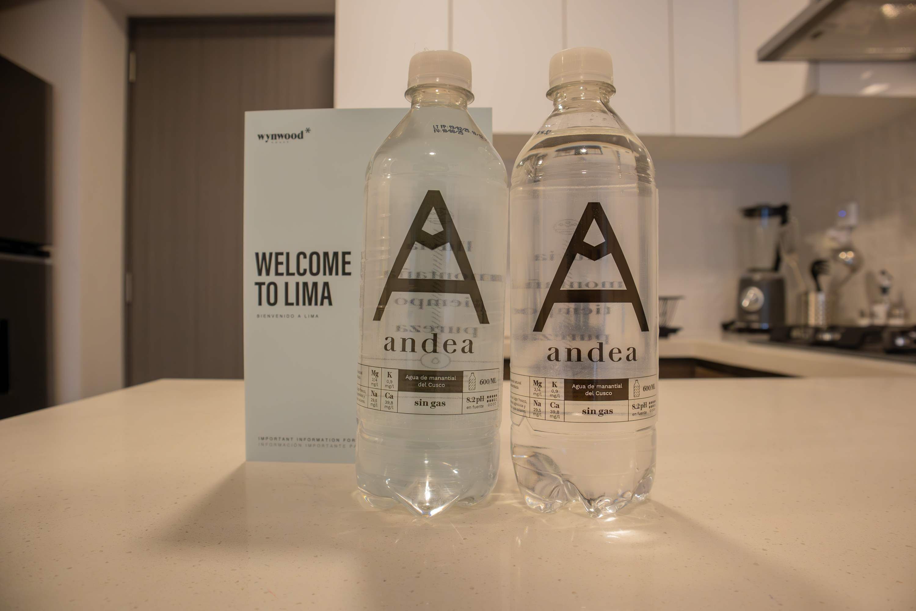 Two bottles of water labeled 'andea' on a kitchen counter with a 'WELCOME TO LIMA' sign in the background.