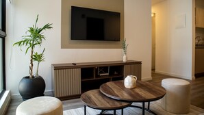 A modern living room with a flat-screen TV, a large potted plant, a wooden coffee table, and a round ottoman. - w Fantastic 2BR w Modern Deco in San Isidro (Lima)