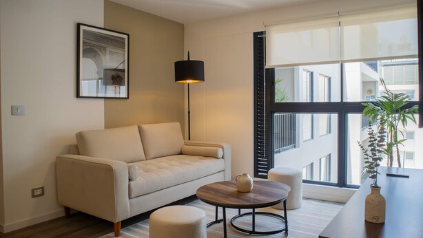 A modern living room with a sofa, a coffee table, and a lamp. There is a window with a view of buildings outside. - w Fantastic 2BR w Modern Deco in San Isidro (Lima)