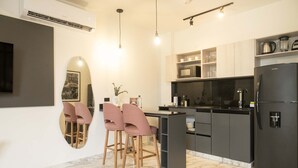 A modern kitchen with a black refrigerator, a microwave, and a sink. There are two pink bar stools and a marble floor.
