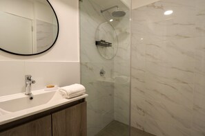 Un bany modern amb dutxa de marbre, un mirall rodó i un lavabo de fusta amb un lavabi.