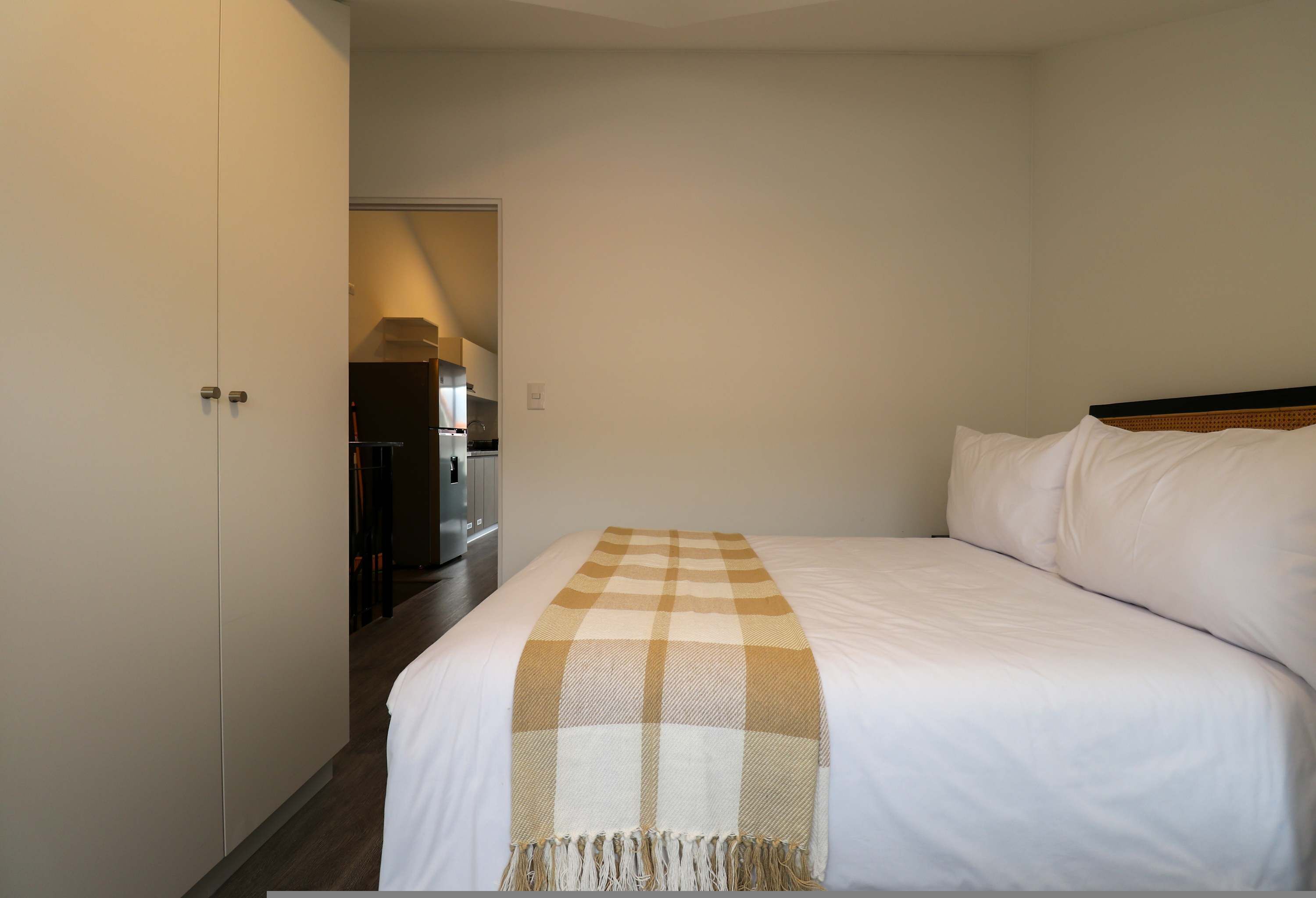 A hotel room with a large bed, a wardrobe, and a kitchenette in the background.