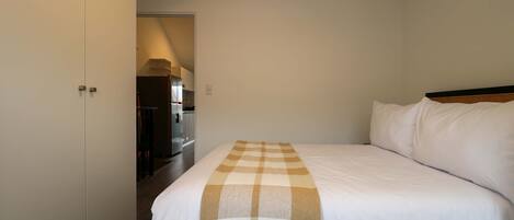 A hotel room with a large bed, a wardrobe, and a kitchenette in the background.