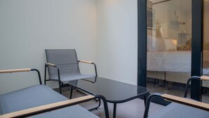 A modern hotel room with a glass partition, a bed with white bedding, a small table, and two chairs with metal frames and fabric seats. - w Spectacular 1BR w Terrace in Miraflores (Lima)