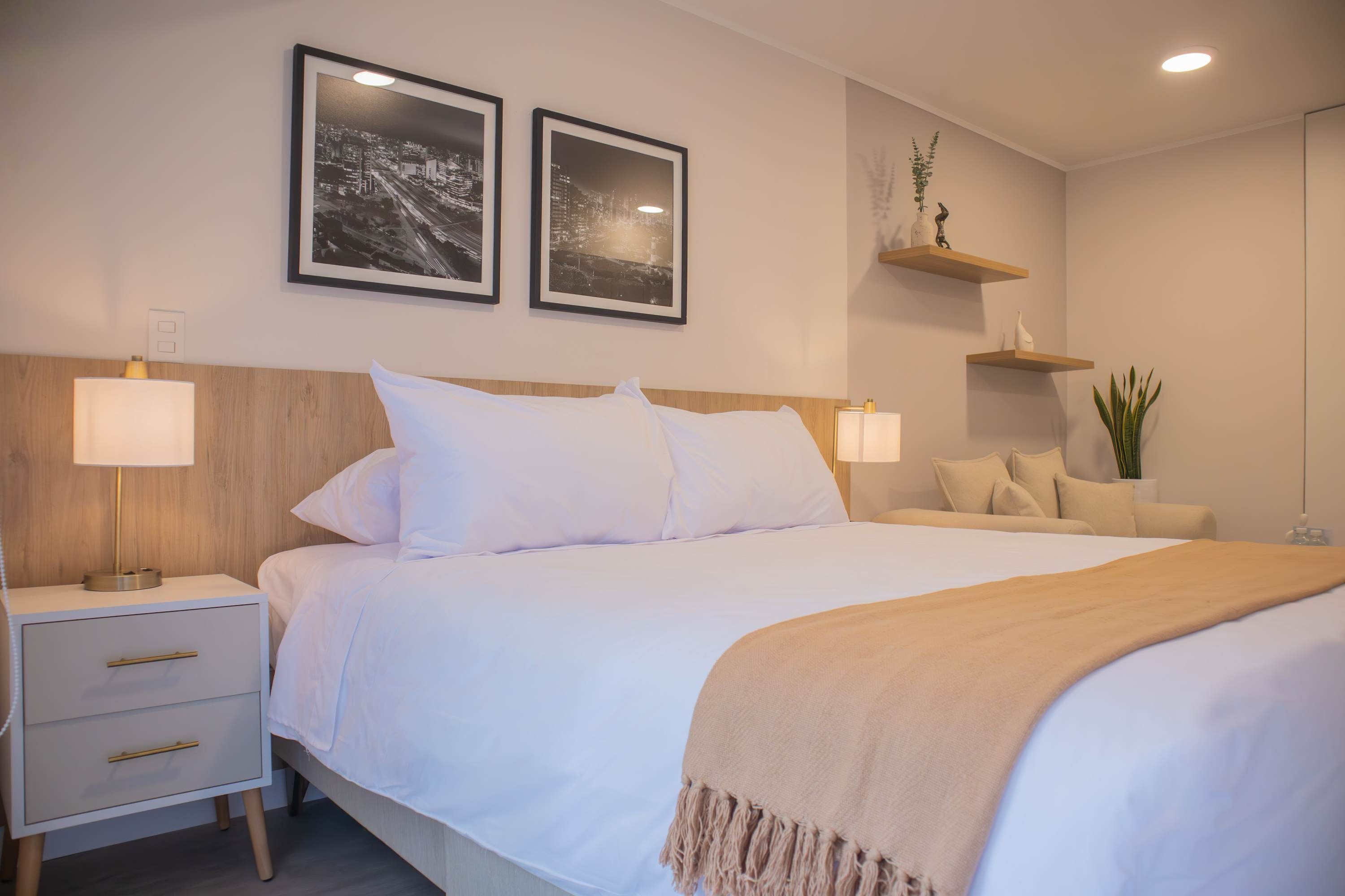 Un dormitorio ordenado con cama, mesitas de noche y estantes en la pared.