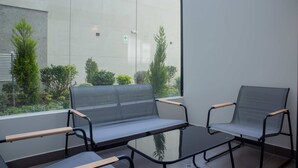 A modern outdoor seating area with two chairs and a table, a glass partition, and a view of greenery and a building in the background. - w Spectacular 1BR w Terrace in Miraflores (Lima)