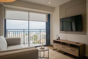 A modern living room with a large window, a flat-screen TV, a sofa, and a wooden TV stand. - w Beautiful 3BR w Balcony in San Isidro (Lima)
