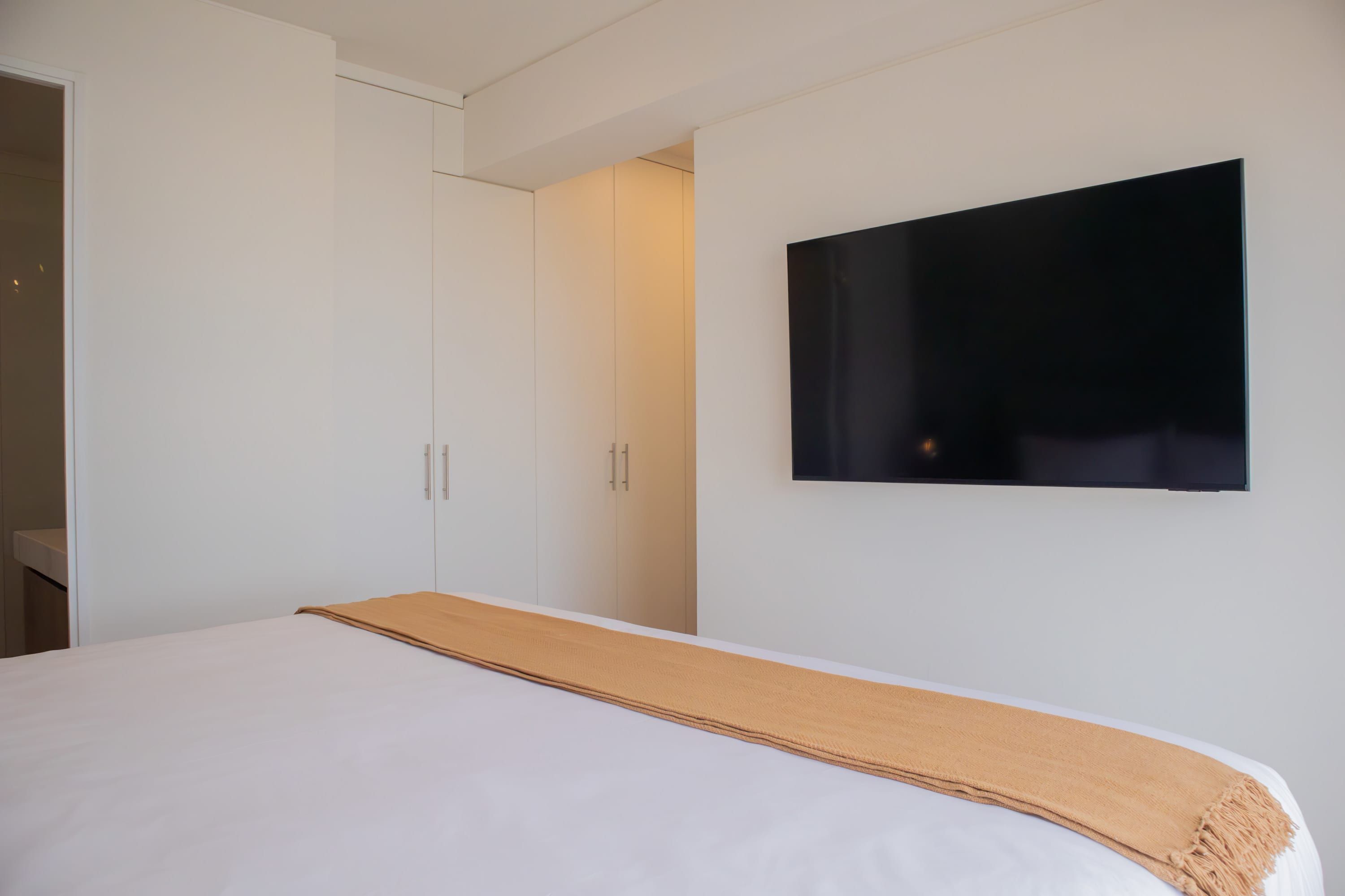 Moderni hotellihuone, jossa on suuri sänky, seinälle asennettu taulutelevisio ja liukuovilla varustettu vaatekaappi.