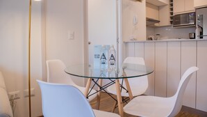 A modern kitchen with white cabinets, a microwave, and a coffee machine. There is a glass table with chairs and a bottle of water on it. - w Amazing 2BR w Balcony in San Isidro (Lima)