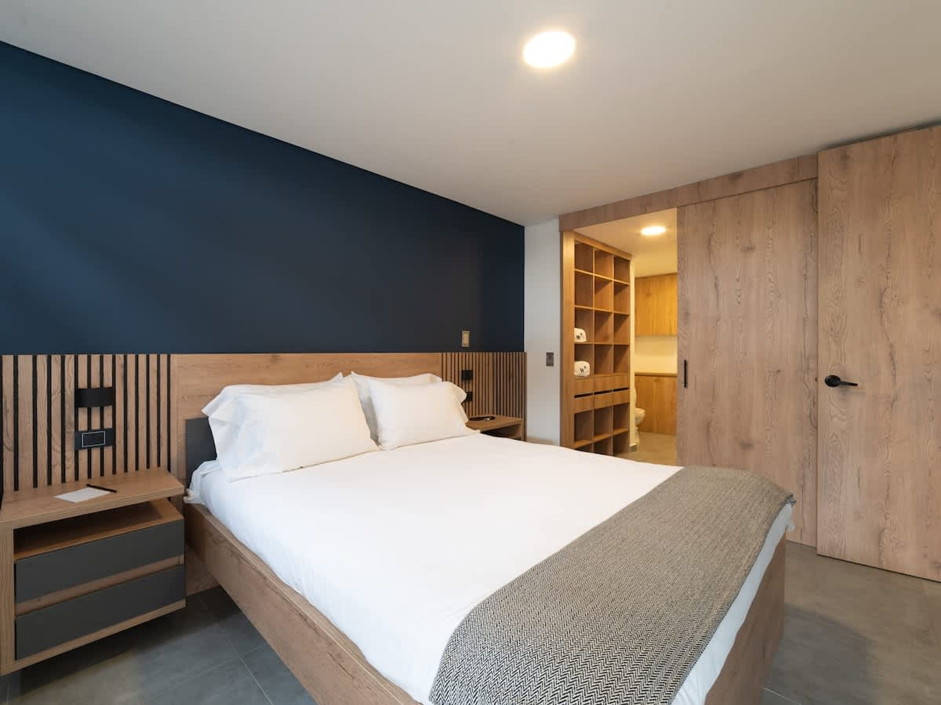 Een moderne slaapkamer met een bed, nachtkastjes, een houten garderobe en een inbouwkast.