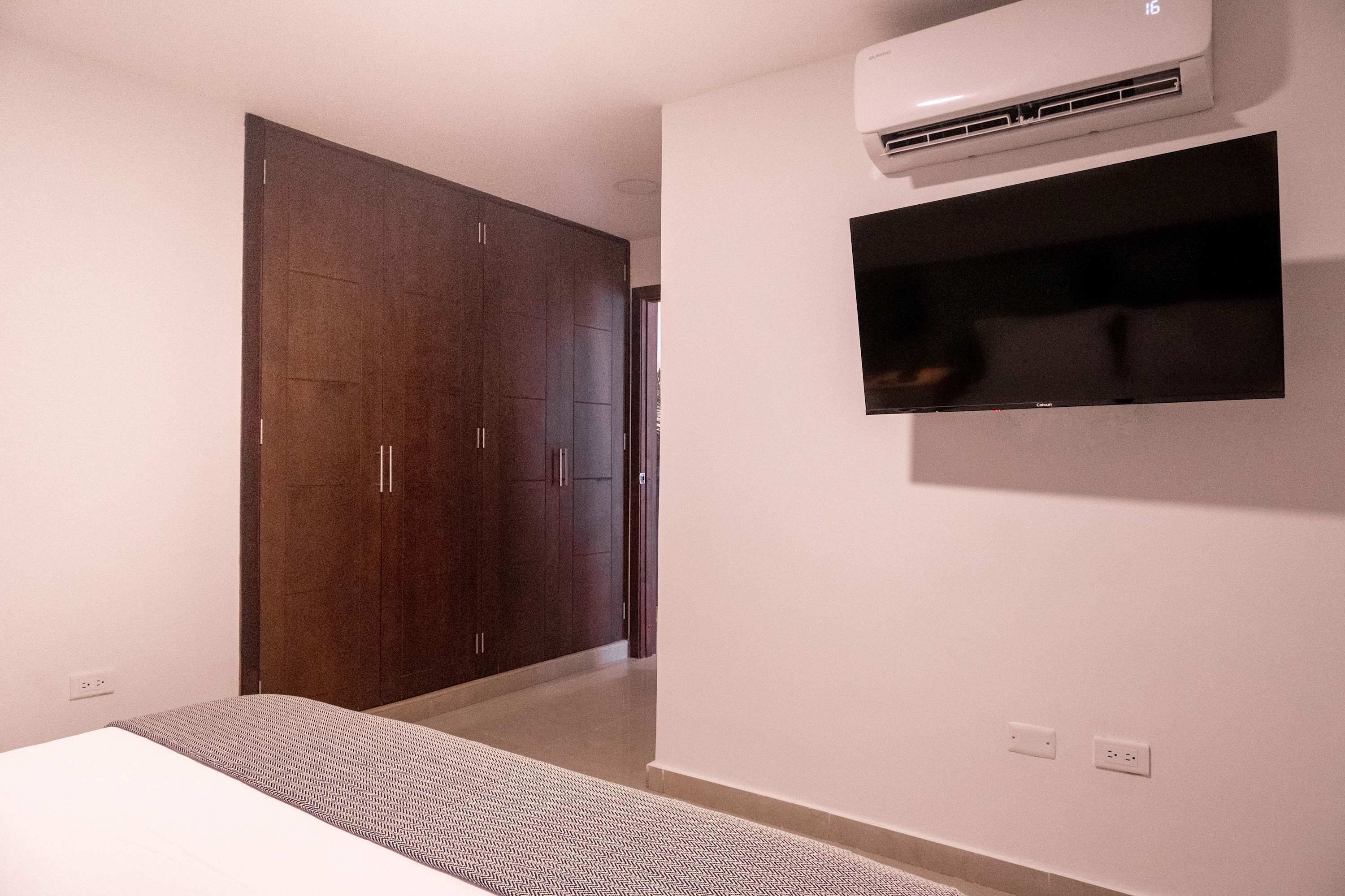 A bedroom with a bed, a wardrobe, an air conditioning unit, and a mounted television.