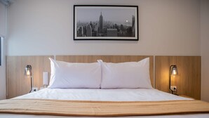 Un lit bien fait, avec du linge de lit blanc, une tête de lit en bois et deux lampes fixées au mur.
