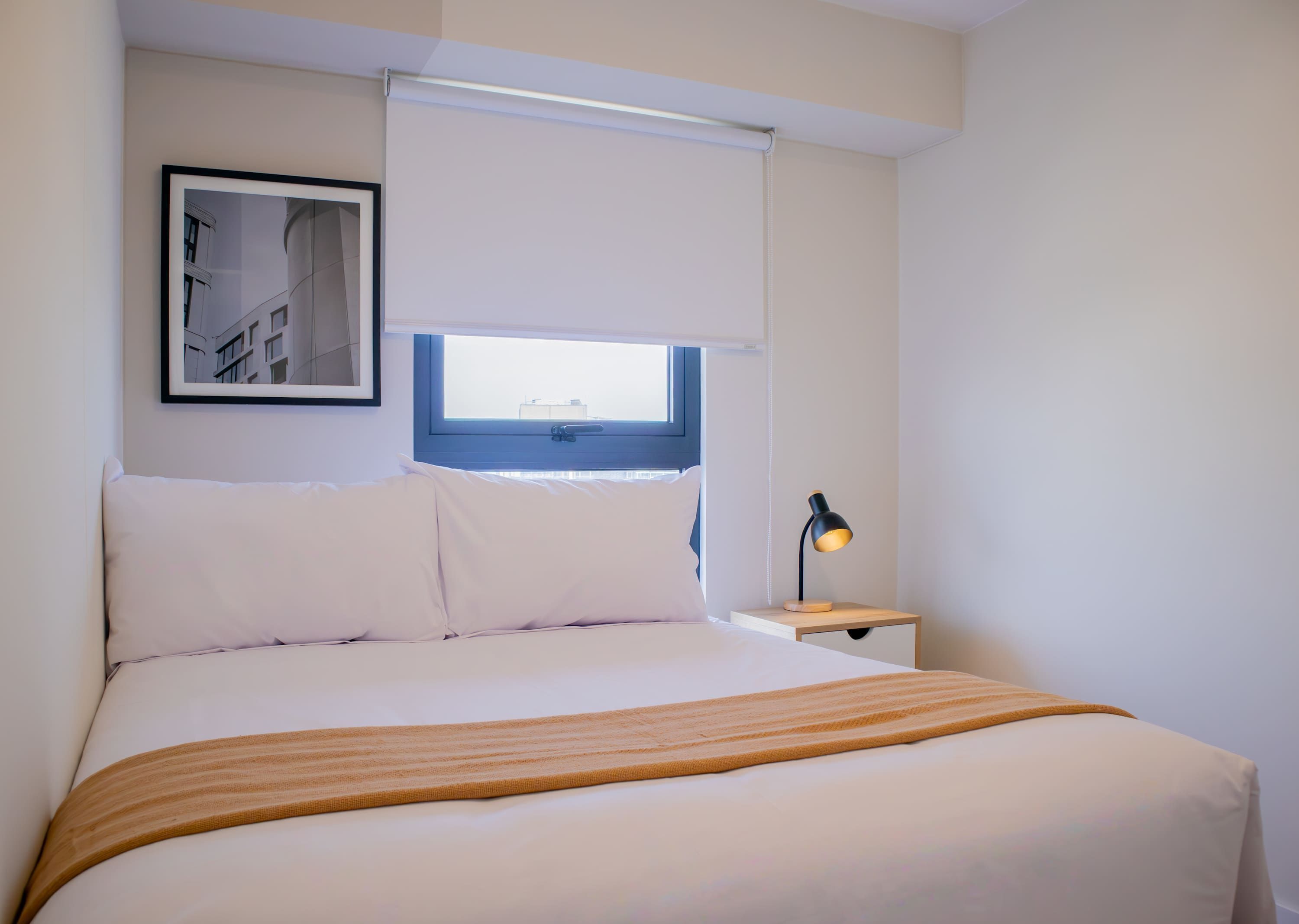 A neatly made bed with a white and orange striped blanket, a bedside lamp, and a framed picture on the wall.