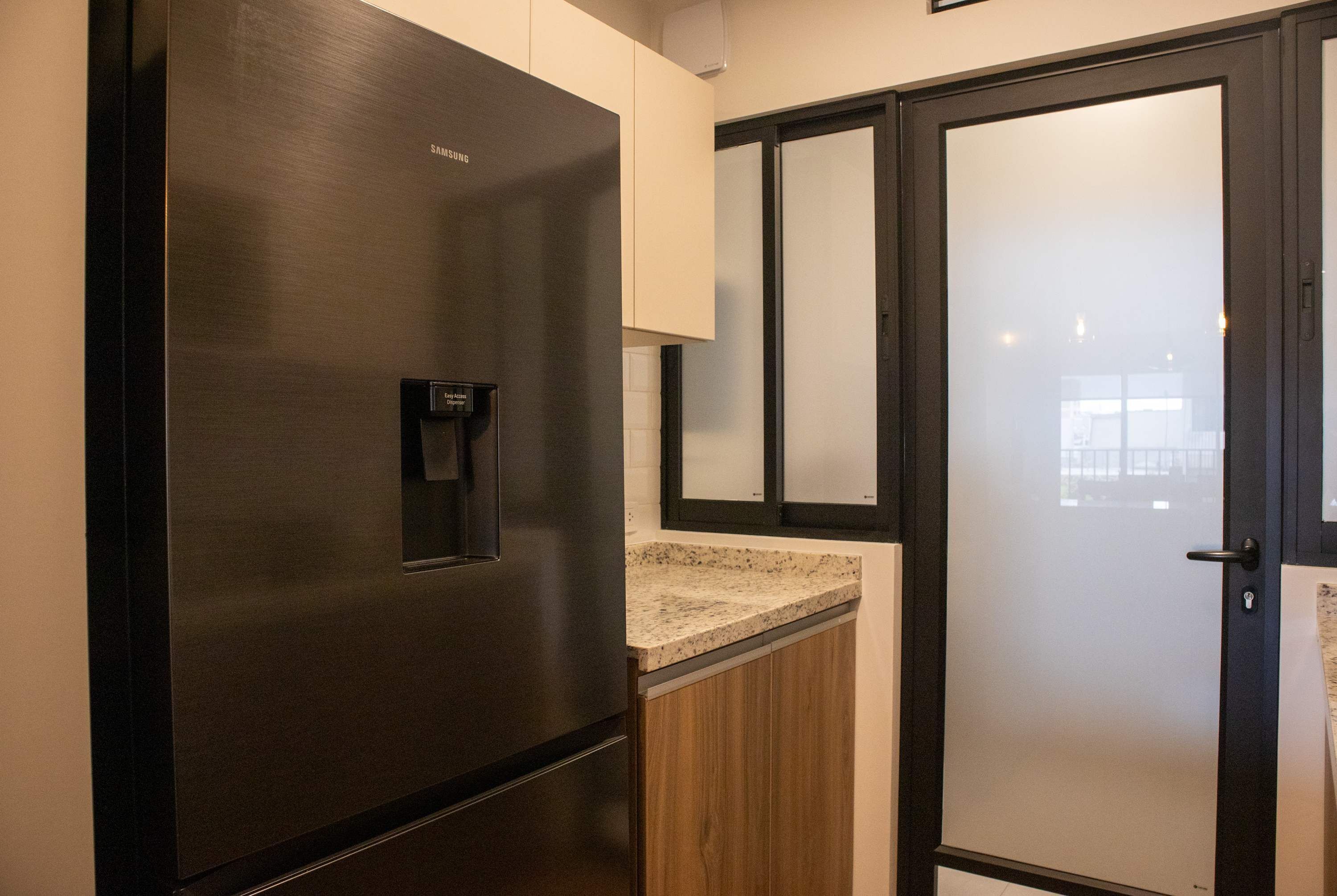 A modern kitchen with a stainless steel refrigerator, wooden cabinets, and a frosted glass door.
