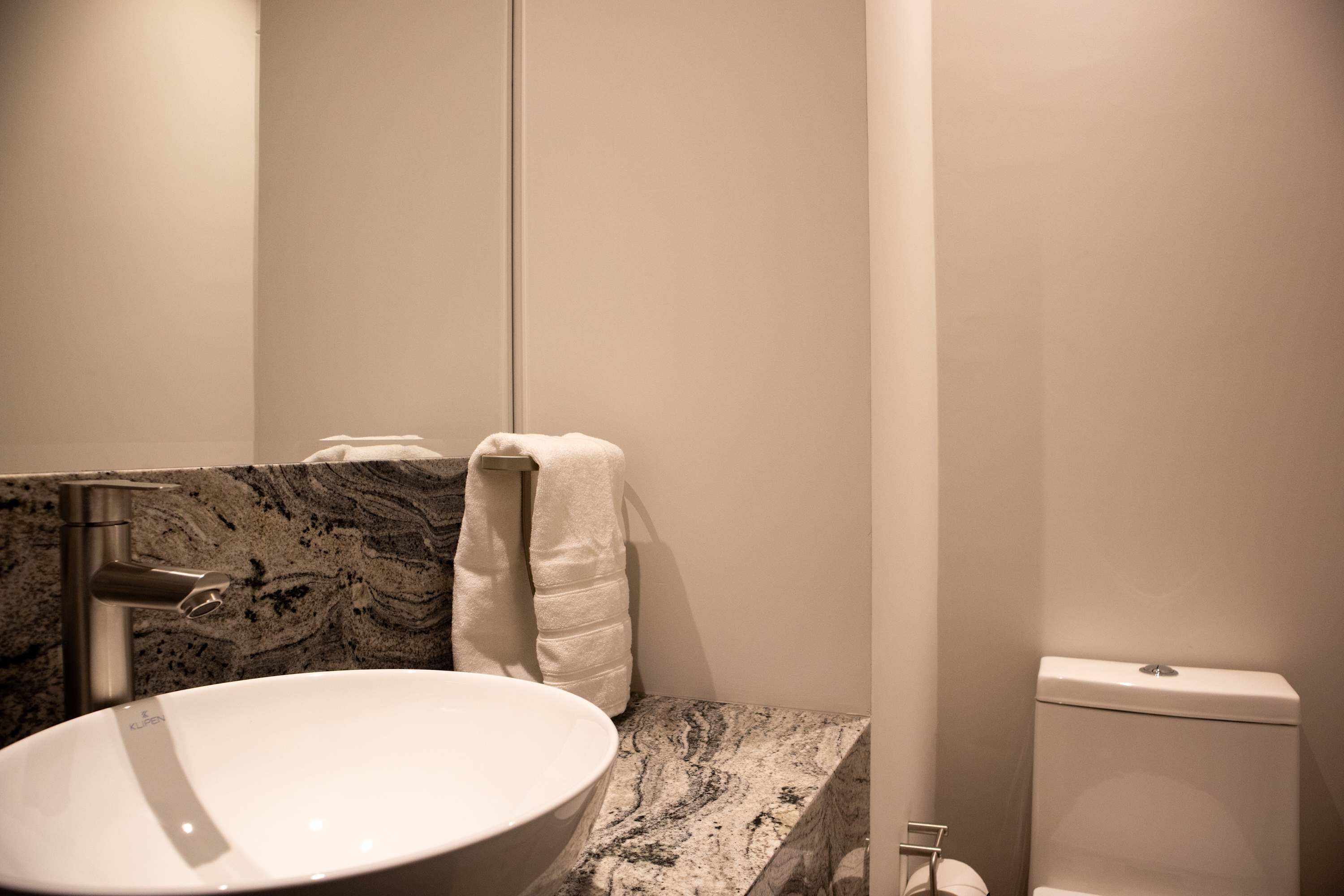 Un baño con un lavabo blanco, encimera de mármol, una toalla colgada en un perchero y un inodoro.