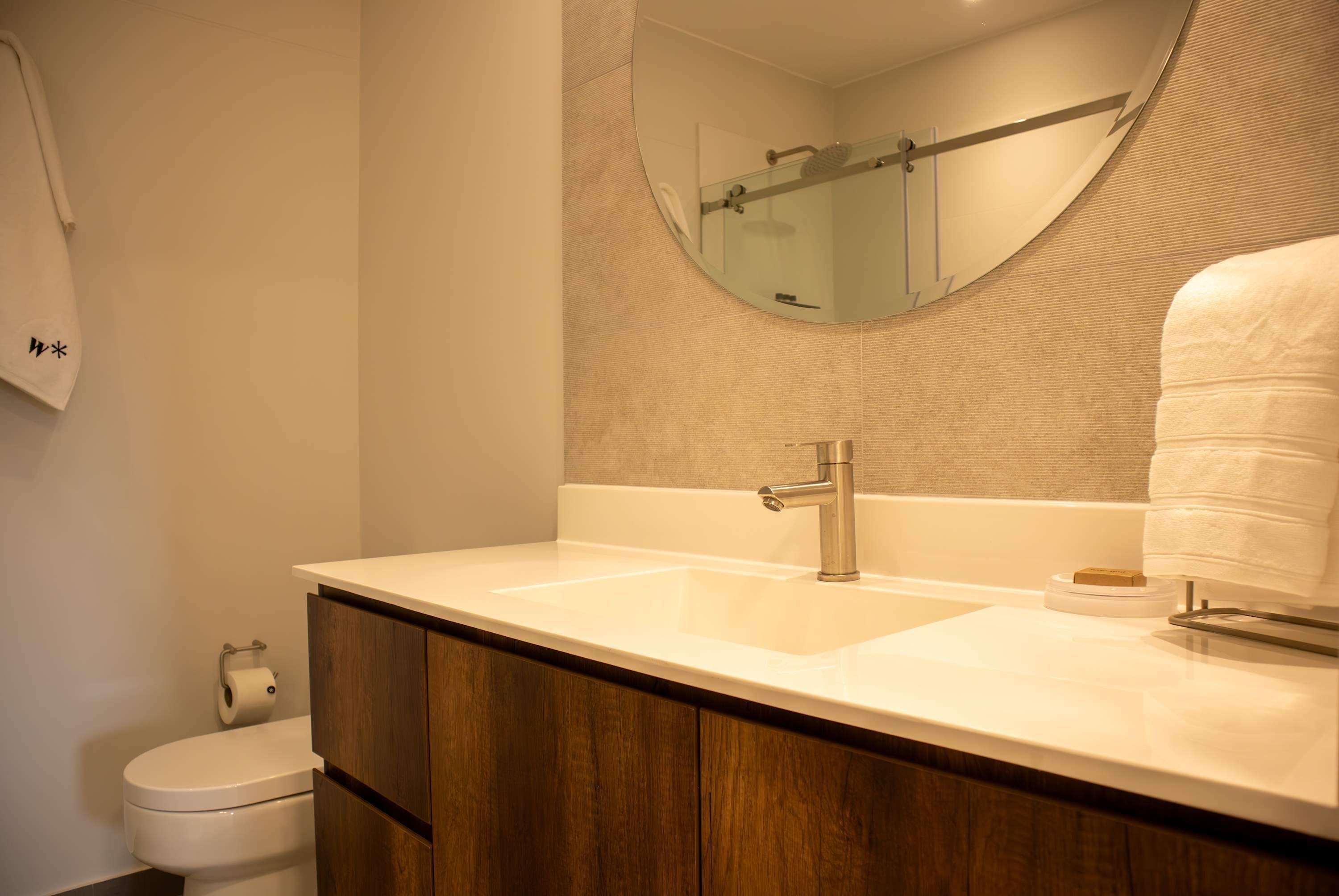 A bathroom with a double sink, wooden cabinets, a toilet, a towel rack, and a mirror.