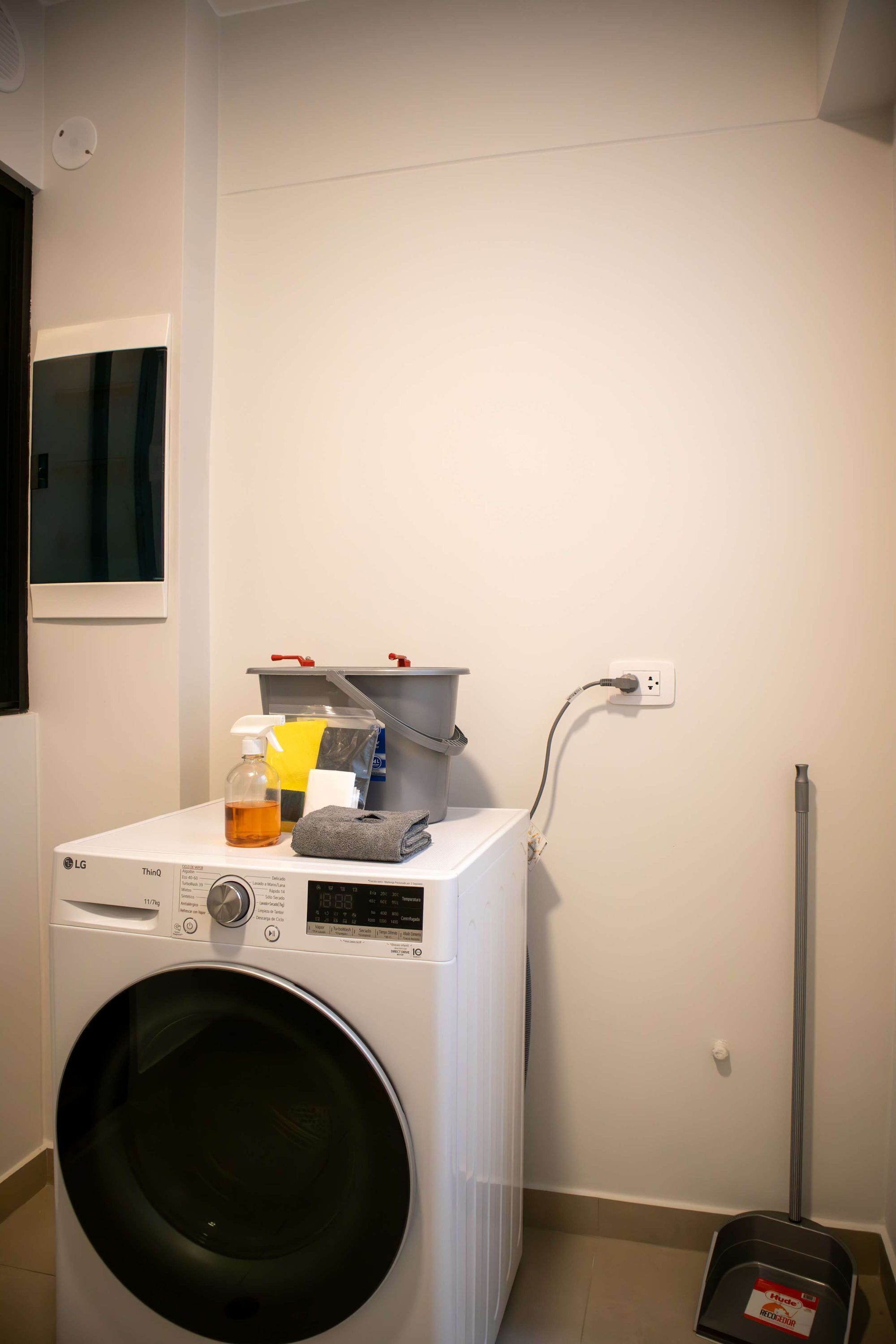 A laundry area with a washing machine, a drying rack, and a vacuum cleaner.