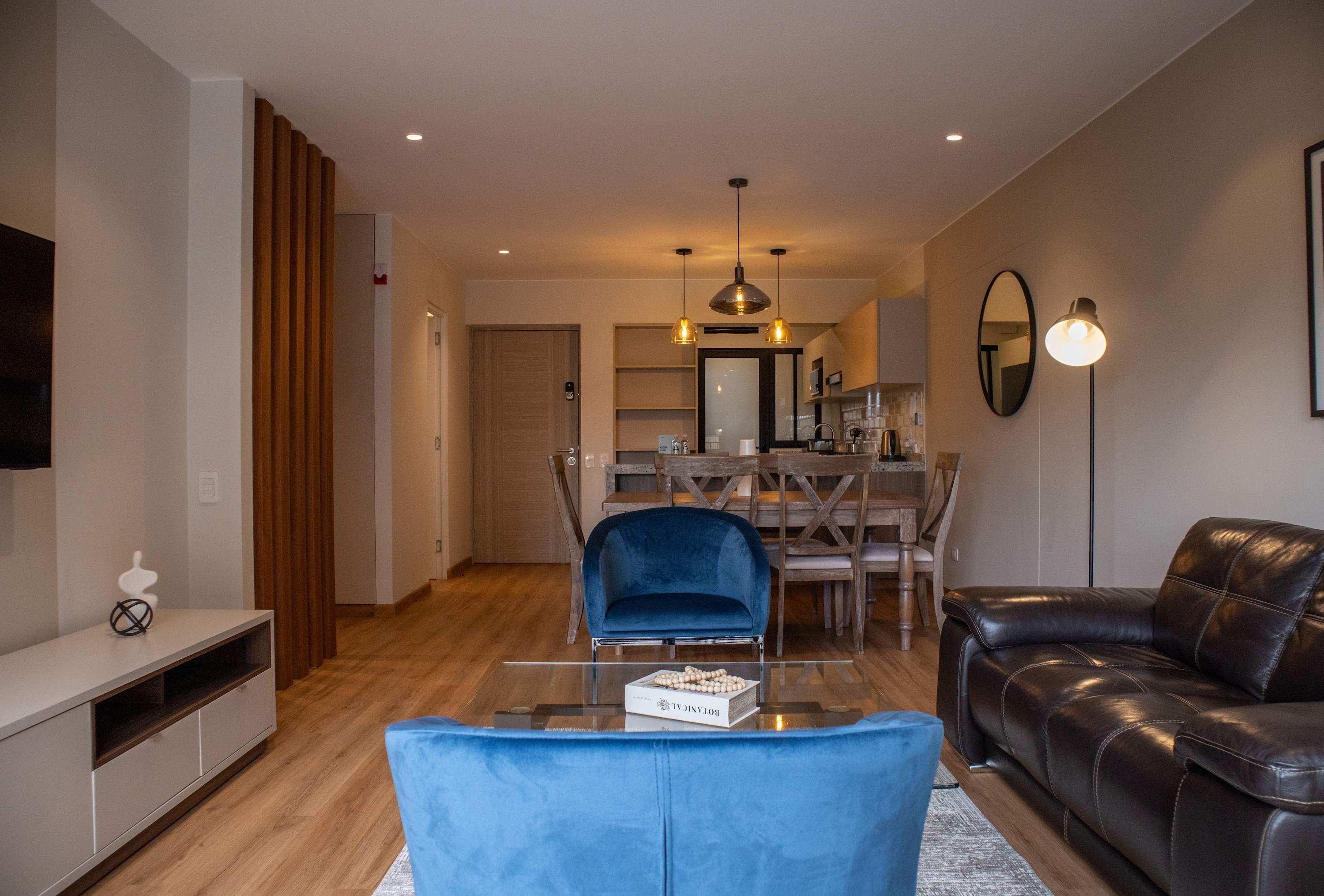 A modern living room with a blue sofa, a black leather couch, and a dining area with wooden chairs and a table.