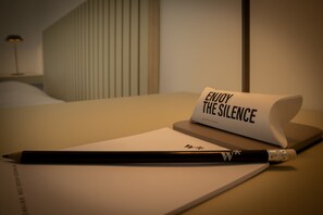 Un escritorio con un lápiz, un papel y una tarjeta doblada que dice 'DISFRUTA DEL SILENCIO' con la palabra 'TAPONES' debajo.