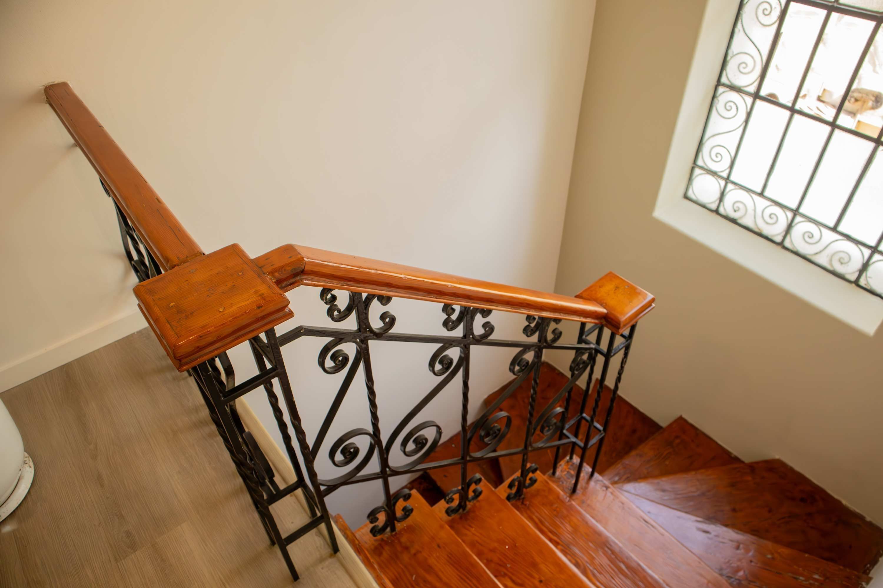 A wooden staircase with a metal railing and a window with decorative bars.