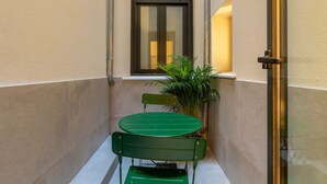 Una petita zona exterior amb una taula, dues cadires, una finestra i una planta en test.