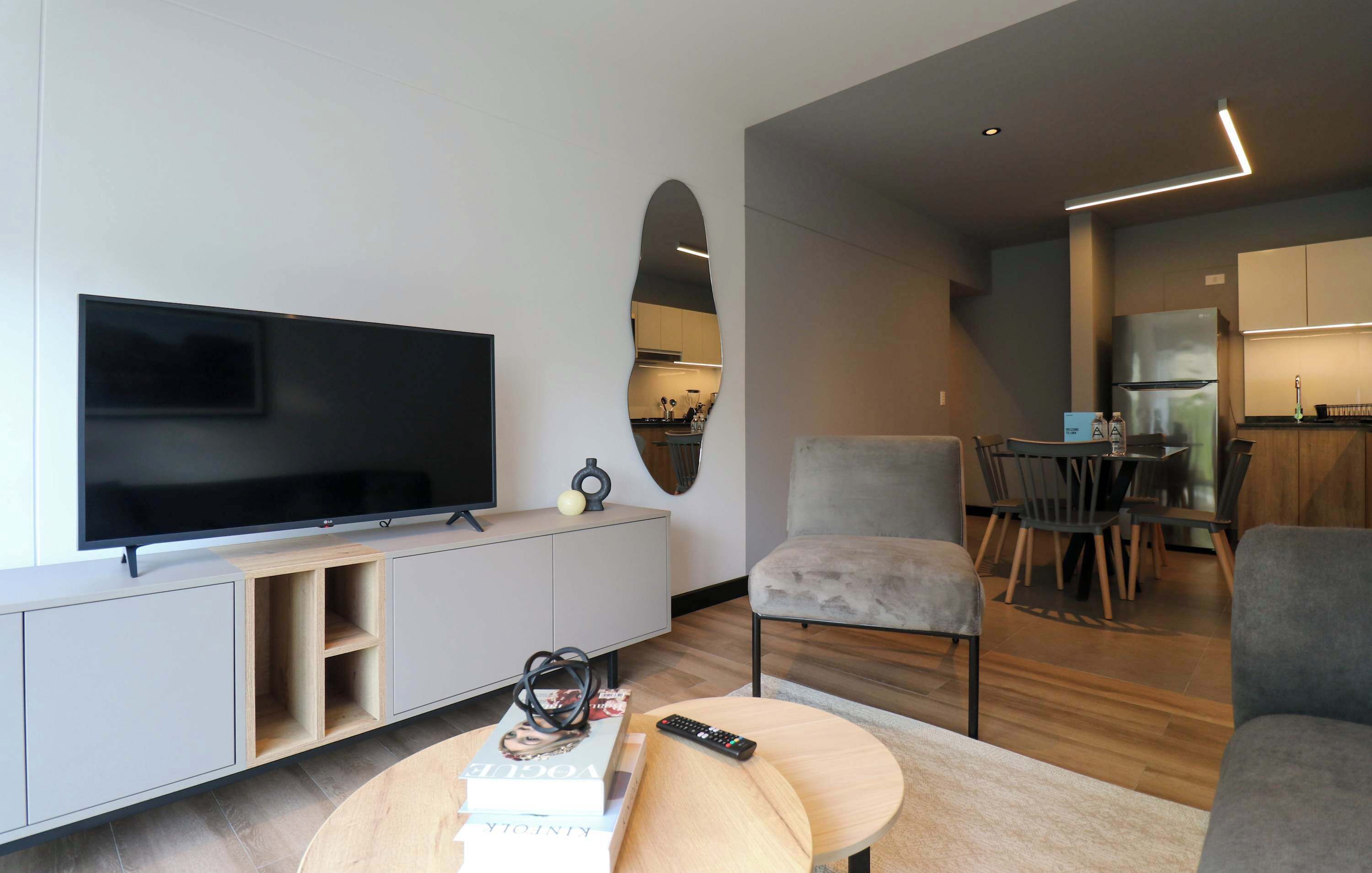 Ett modernt vardagsrum med en platt-TV, en soffa, ett soffbord och en matplats med stolar och ett bord.