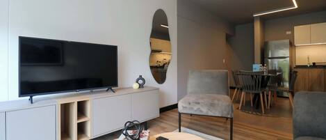 Ett modernt vardagsrum med en platt-TV, en soffa, ett soffbord och en matplats med stolar och ett bord.