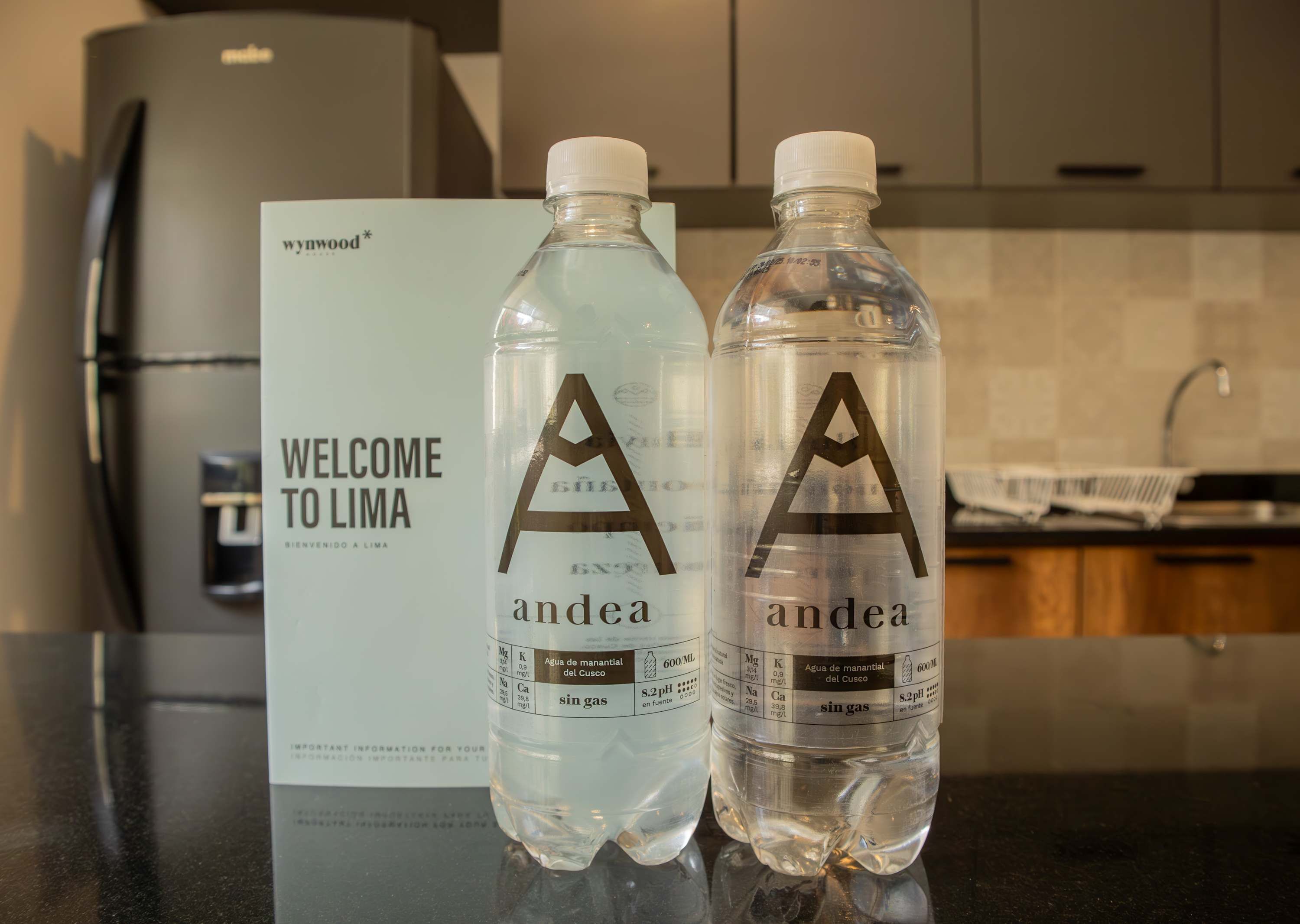 Two water bottles with the brand name 'andea' and a welcome sign for 'Lima' in the background.