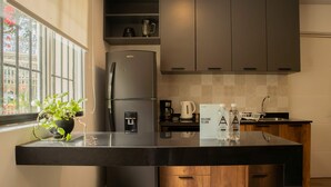 A modern kitchen with a built-in refrigerator, a coffee maker, and a water dispenser. There is a welcome sign and two water bottles on the counter.