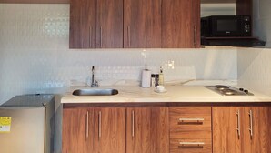 A kitchen with wooden cabinets, a stainless steel sink, a microwave, and a stove. - w Stunning 1BR in Laureles (Medellín)
