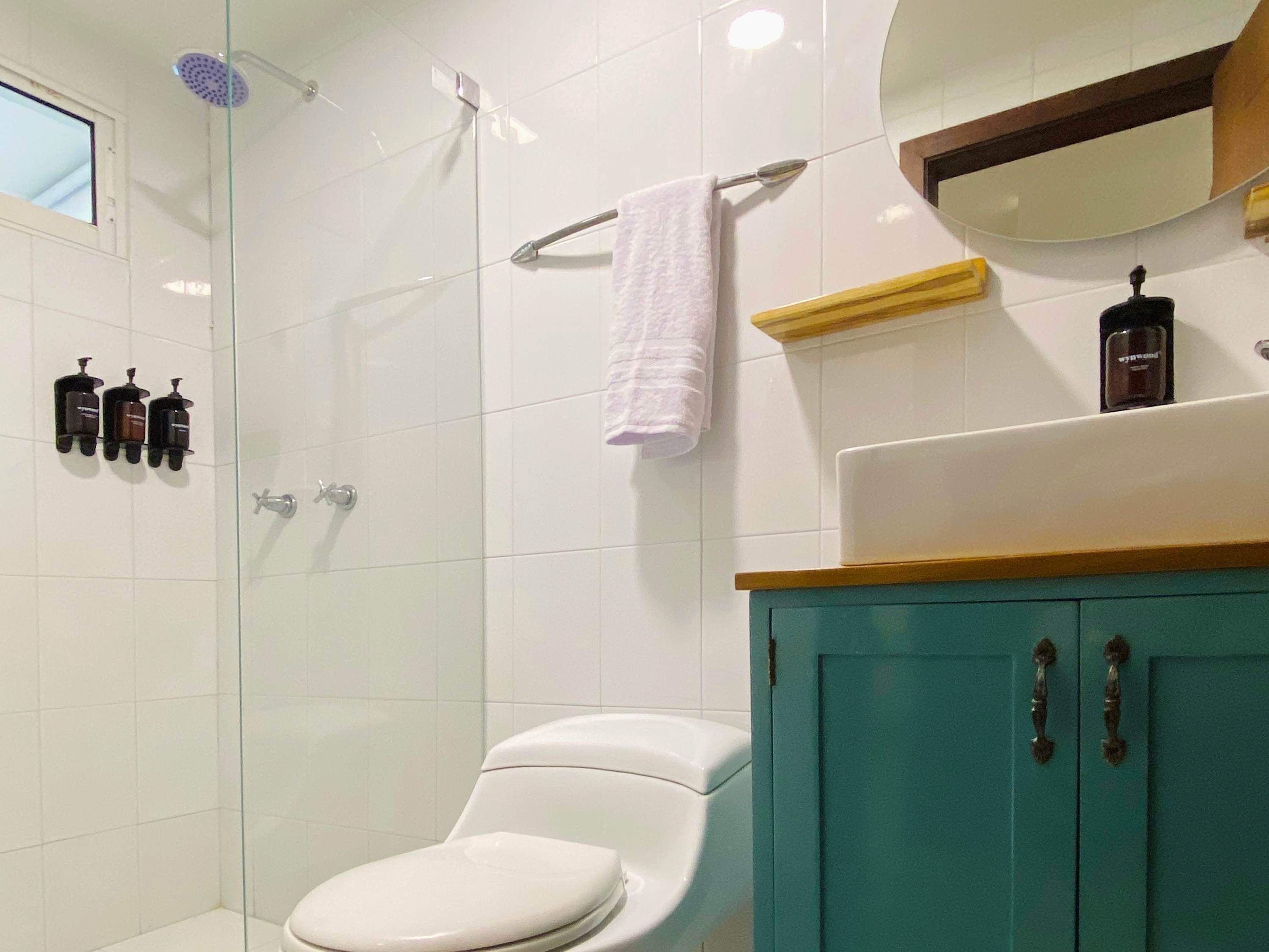 A bathroom with a white toilet, a glass-enclosed shower, and a teal cabinet with a mirror above it.