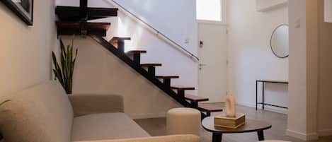 A modern living room with a staircase, a sofa, a coffee table, and a potted plant.