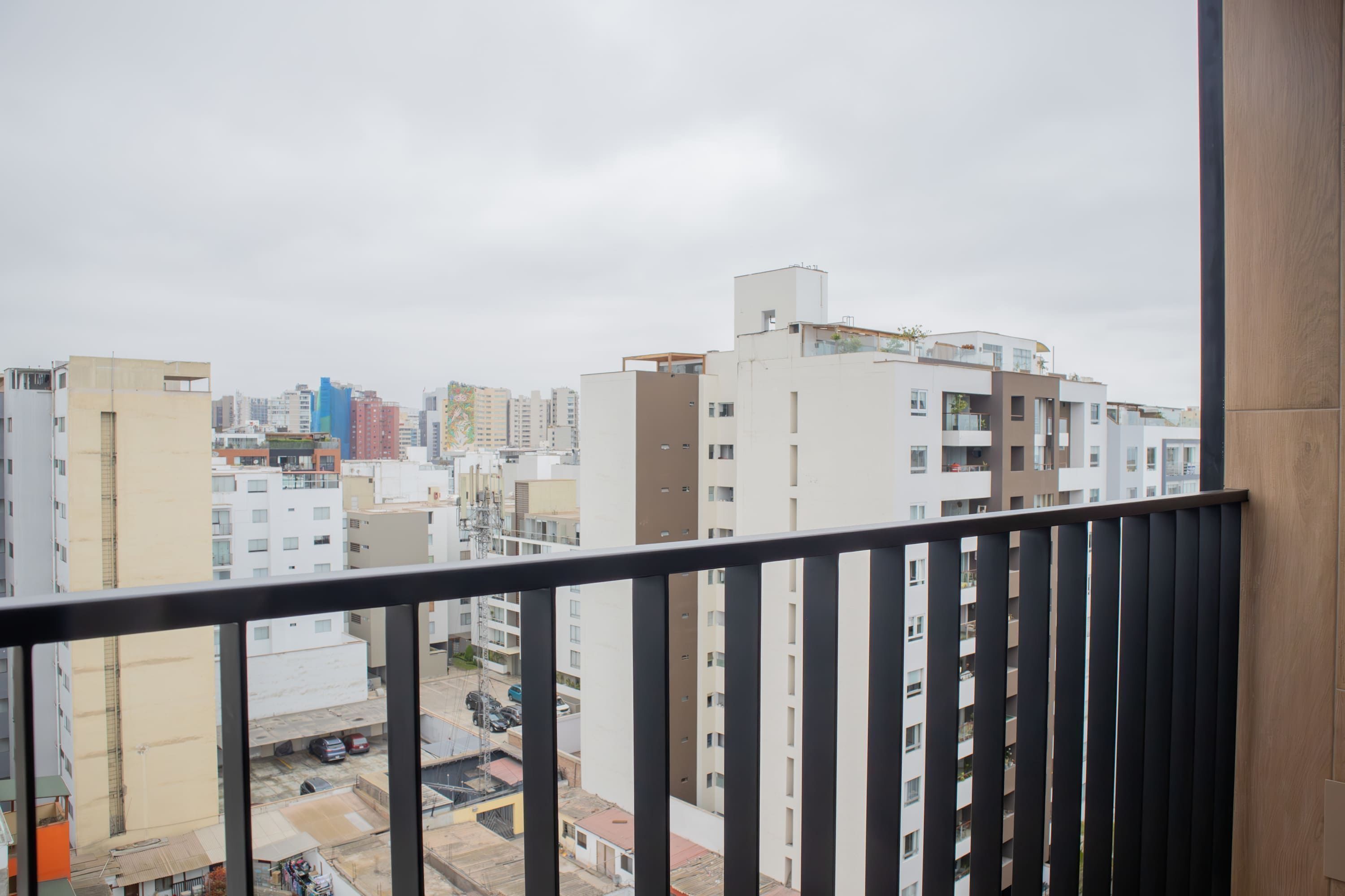 Une vue depuis un balcon donnant sur un paysage urbain, avec des bâtiments modernes et un ciel dégagé.
