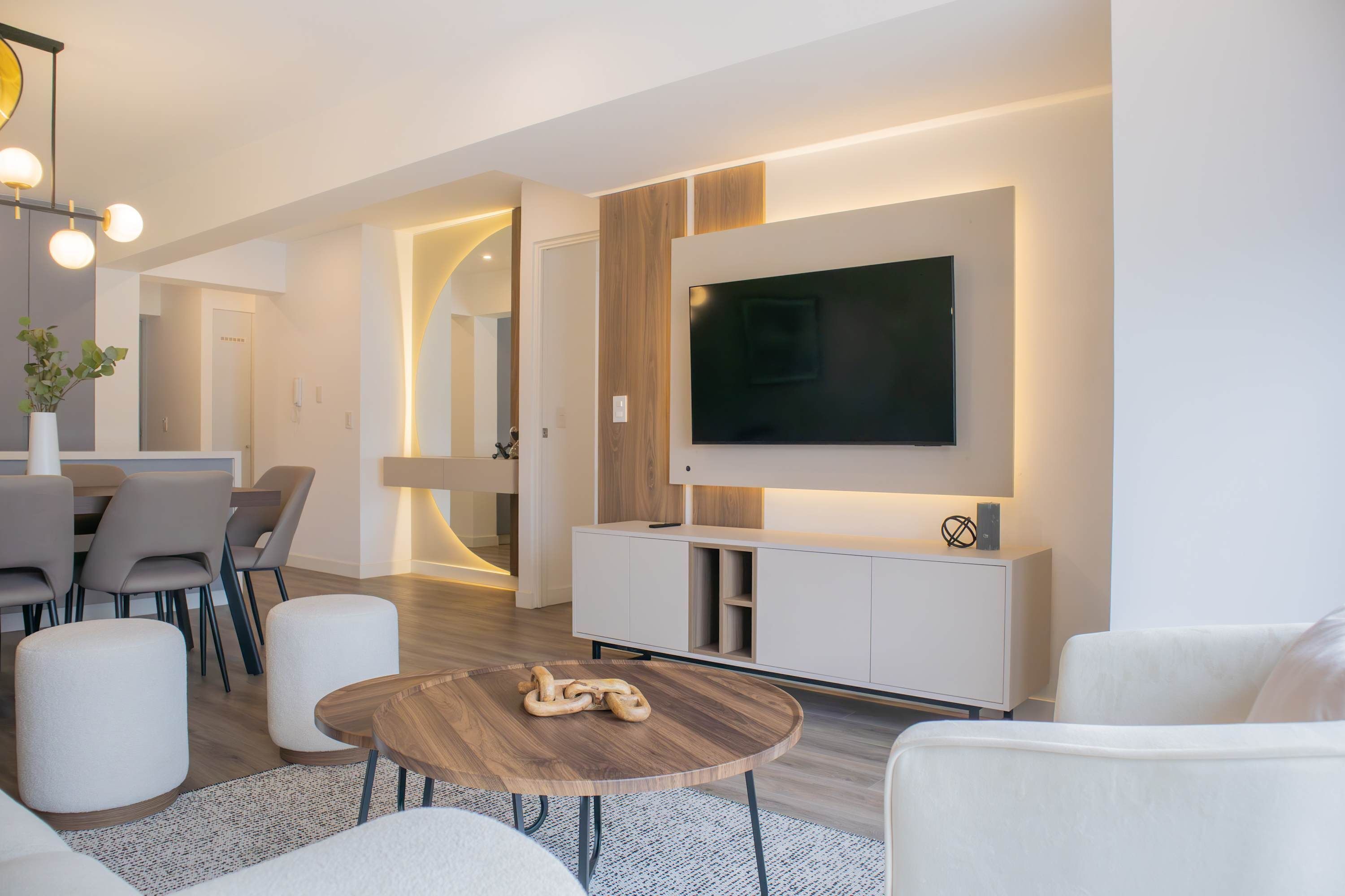Een moderne woonkamer met een flatscreen televisie aan de muur, een houten salontafel en een witte bank.