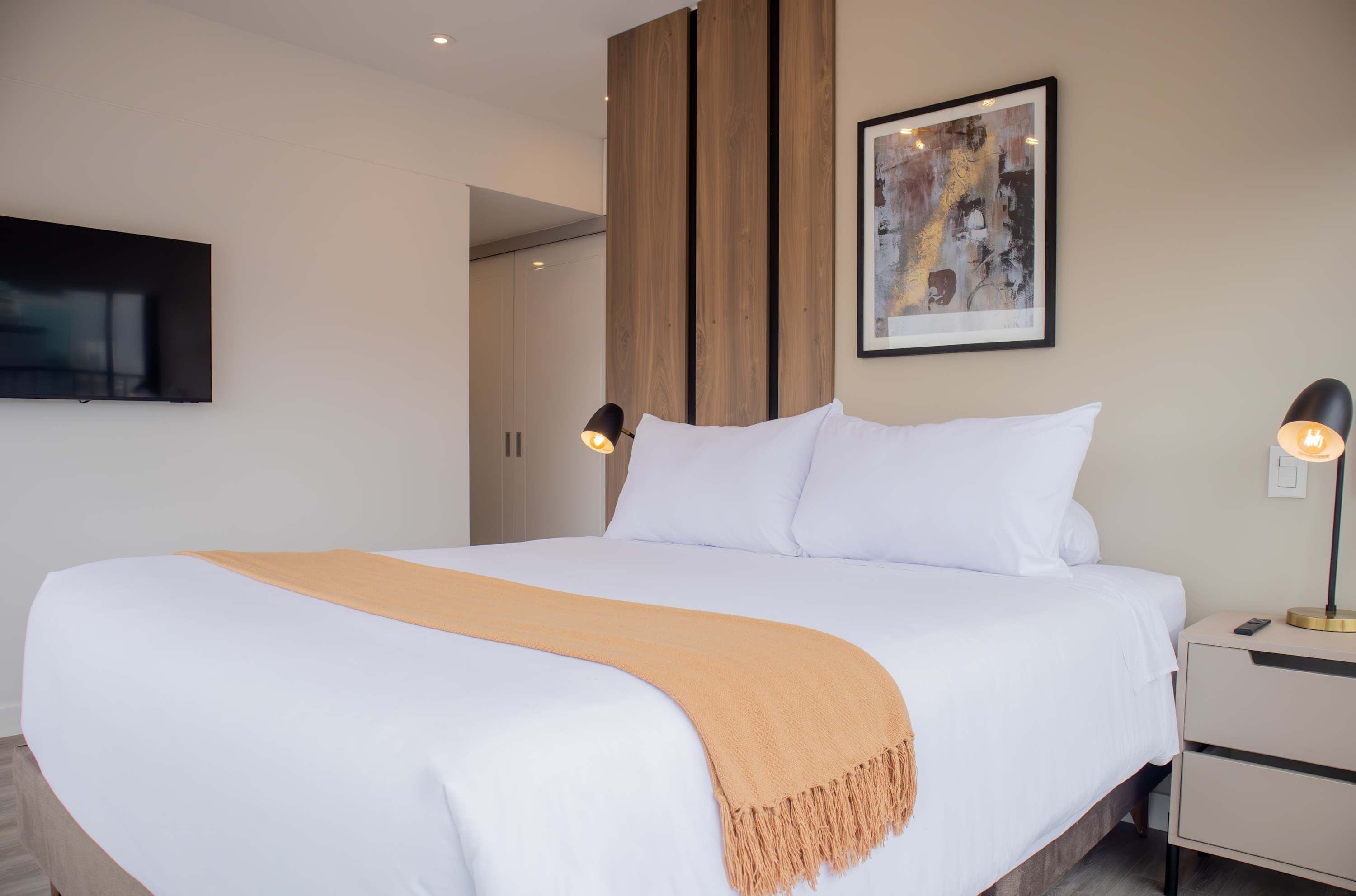Een moderne hotelkamer met een groot bed, een nachtkastje met een lamp en een lijst met een abstract schilderij aan de muur.